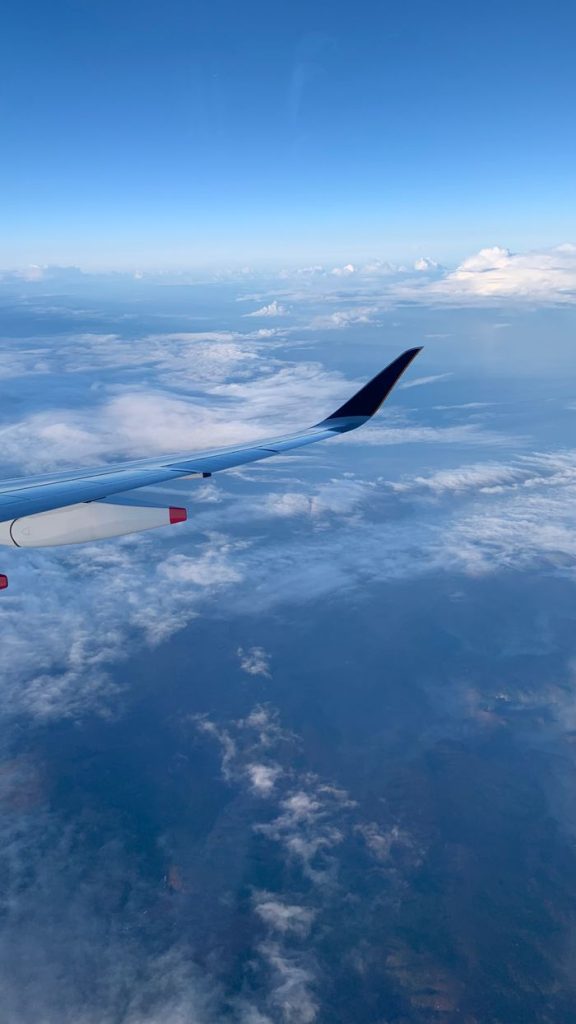 View of clouds and distant land from an airplane, showcasing the beauty of aerial travel.