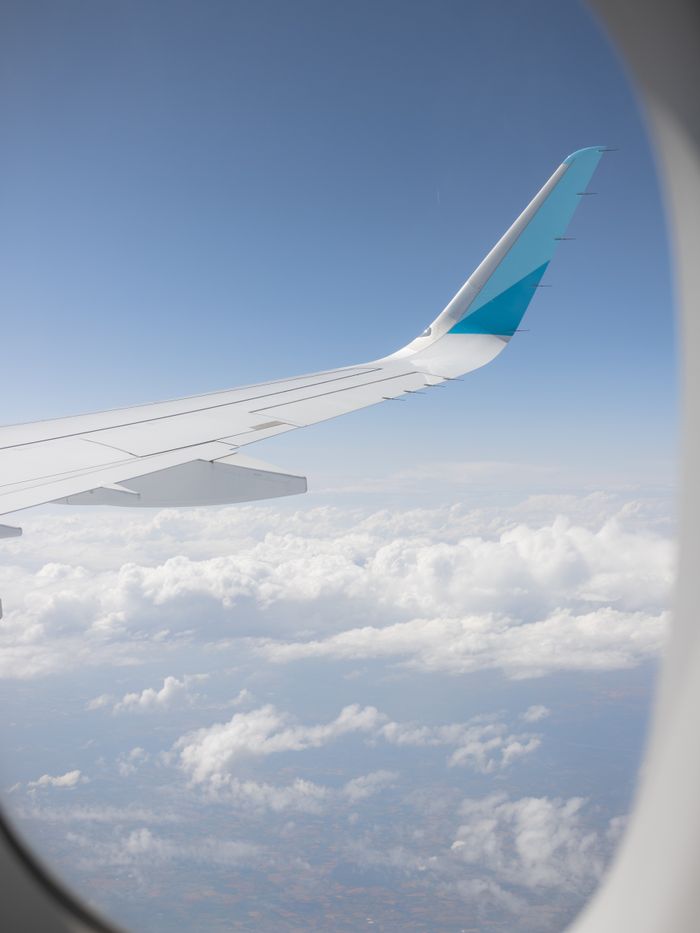 Aerial view of sky and clouds from airplane window, highlighting the wing of the aircraft.
